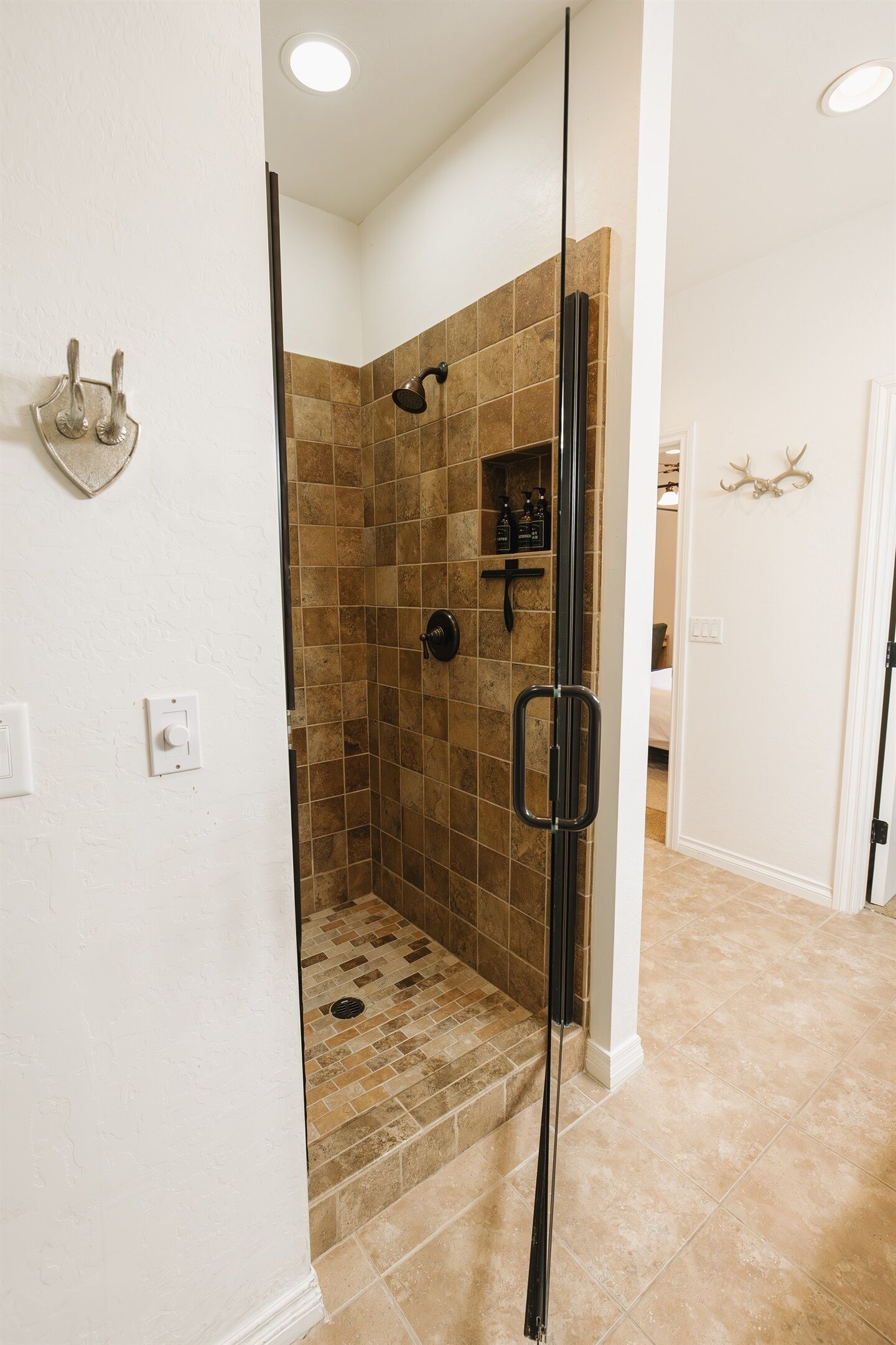 A walk-in shower with a glass door, tiled walls, and a small shelf with toiletries.