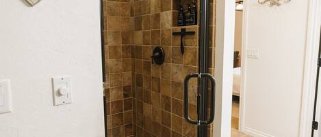 A walk-in shower with a glass door, tiled walls, and a small shelf with toiletries.