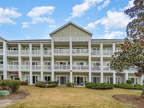 Exterior of the three-story building with white balconies and landscaped grounds.