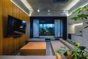 Una sala de estar moderna con un televisor de pantalla plana, un sofá, una mesa de centro y un ventanal con vistas a zonas verdes.