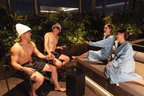 Un grupo de personas sentadas en un espacio interior moderno con vistas al cielo nocturno a través de amplios ventanales, rodeado de plantas de interior.