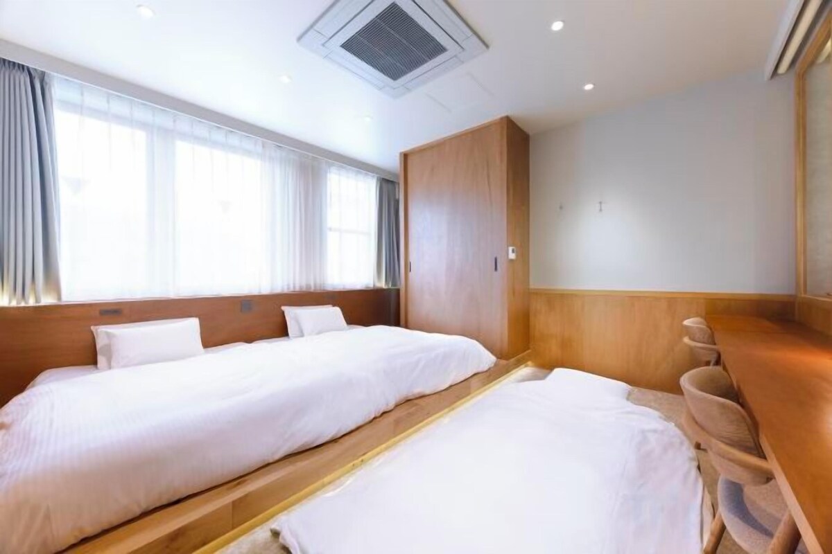 Una habitación de hotel con dos camas, un armario de madera y una ventana con cortinas.