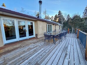 A wooden deck with a glass table and chairs, a covered patio area, and a chimney. - Luxury Angel Fire 5BR 4B, Views!, Game Room (Angel Fire)