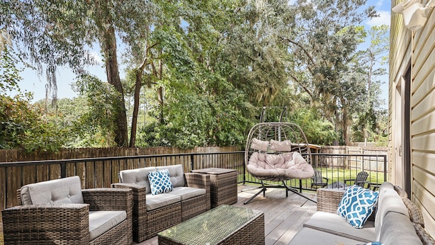 Un patio al aire libre con mobiliario de mimbre, incluyendo sofás y sillones, y una silla colgante.