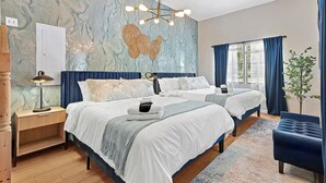 Un dormitorio con dos camas, una mesita de noche de madera, una lámpara, una pared decorativa y una ventana con cortinas.