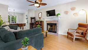 Una sala de estar con sofá, un sillón de cuero marrón, chimenea, ventilador de techo y televisor.