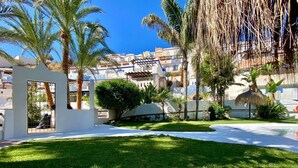 A well-maintained outdoor area with a grassy lawn, palm trees, and a white building with a window. - "Rincon de Marinos", a spacious house in a quiet estate, 5 mins. from the beach (Almuñécar)