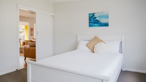 Un dormitorio con una cama blanca, un cuadro de una ola y una puerta que da a otra habitación.