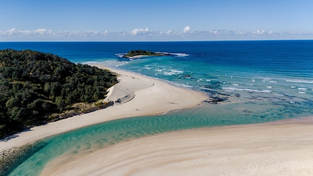 Un paisaje costero con una playa arenosa, aguas turquesas cristalinas y una zona boscosa.