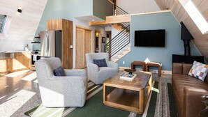 A spacious living area with a high ceiling, a staircase, a kitchen, and a fireplace. - New A-Frame in wine country (Lake Leelanau)