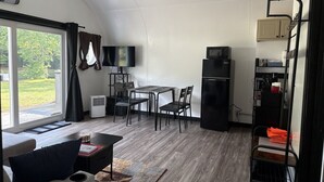 Un espacio habitable compacto con comedor, kitchenette y un amplio ventanal con vista a zonas verdes.