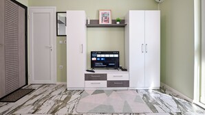 A room with a TV on a cabinet, a door, and a patterned rug. - New Modern 1 bedroom with private parking (Varna)