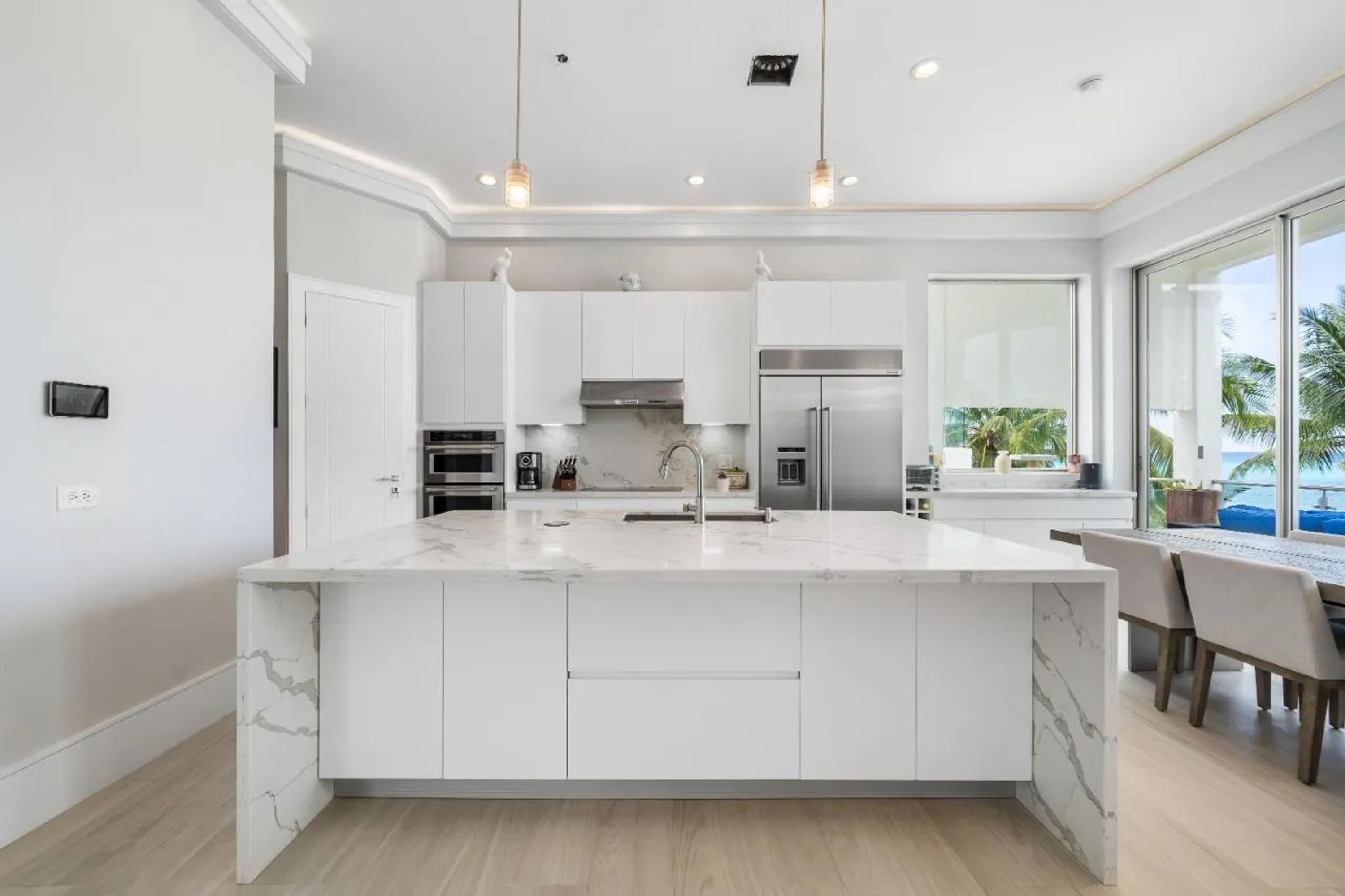 A modern kitchen with white cabinetry, a marble island, stainless steel appliances, and pendant lighting.