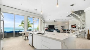 Et moderne køkken med en stor ø, et spiseområde med havudsigt og en trappe, der fører til en etage ovenpå.