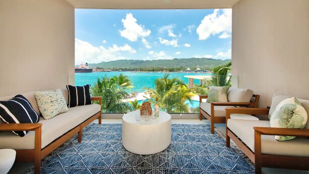 A balcony with a view of the ocean and mountains, furnished with a sofa, chairs, and a coffee table. - Luxury Oceanfront Residence Condo at Soleil Residences (Montego Bay)