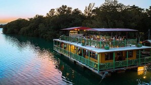A riverboat with outdoor seating and a covered area, surrounded by trees. - Luxury Oceanfront Residence Condo at Soleil Residences (Montego Bay)