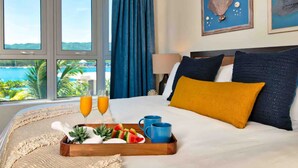 A hotel room with a bed, a tray with fruits and drinks, and a view of the sea. - Luxury Oceanfront Residence Condo at Soleil Residences (Montego Bay)