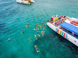 Een boot met de naam "CHUKKA" en de tekst "IT'S TIME TO PLAY" erop, omgeven door helder turquoise water.