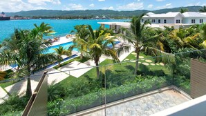 A resort with a pool, palm trees, and a view of the sea. - Luxury Oceanfront Residence Condo at Soleil Residences (Montego Bay)