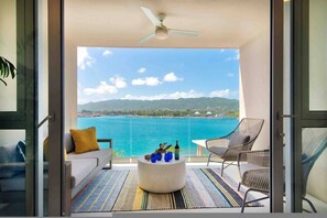 A balcony with a view of the sea, a round coffee table with decorative items, and a ceiling fan.