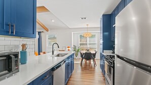 Una cocina moderna con armarios azules, un refrigerador de acero inoxidable y un comedor con mesa y sillas.