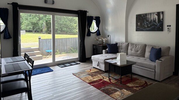 A modern living room with a sofa, coffee table, and a dining area with a table and chairs. - Private Earth Home Retreat, mini goats, fire pits and more - unit A (Littleton)