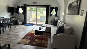 A compact living space with a sofa, a coffee table, a TV, and a dining area. - Private Earth Home Retreat, mini goats, fire pits and more - unit A (Littleton)