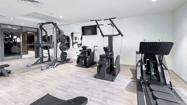 Une salle de sport moderne équipée de divers appareils d’exercice, notamment un banc, des appareils de musculation et un tapis de course.