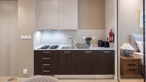 Une cuisine moderne équipée d’une cuisinière à gaz, d’un évier et de meubles de rangement en bois. On y trouve une petite table d’appoint en bois, sur laquelle sont posés une lampe et un objet décoratif.