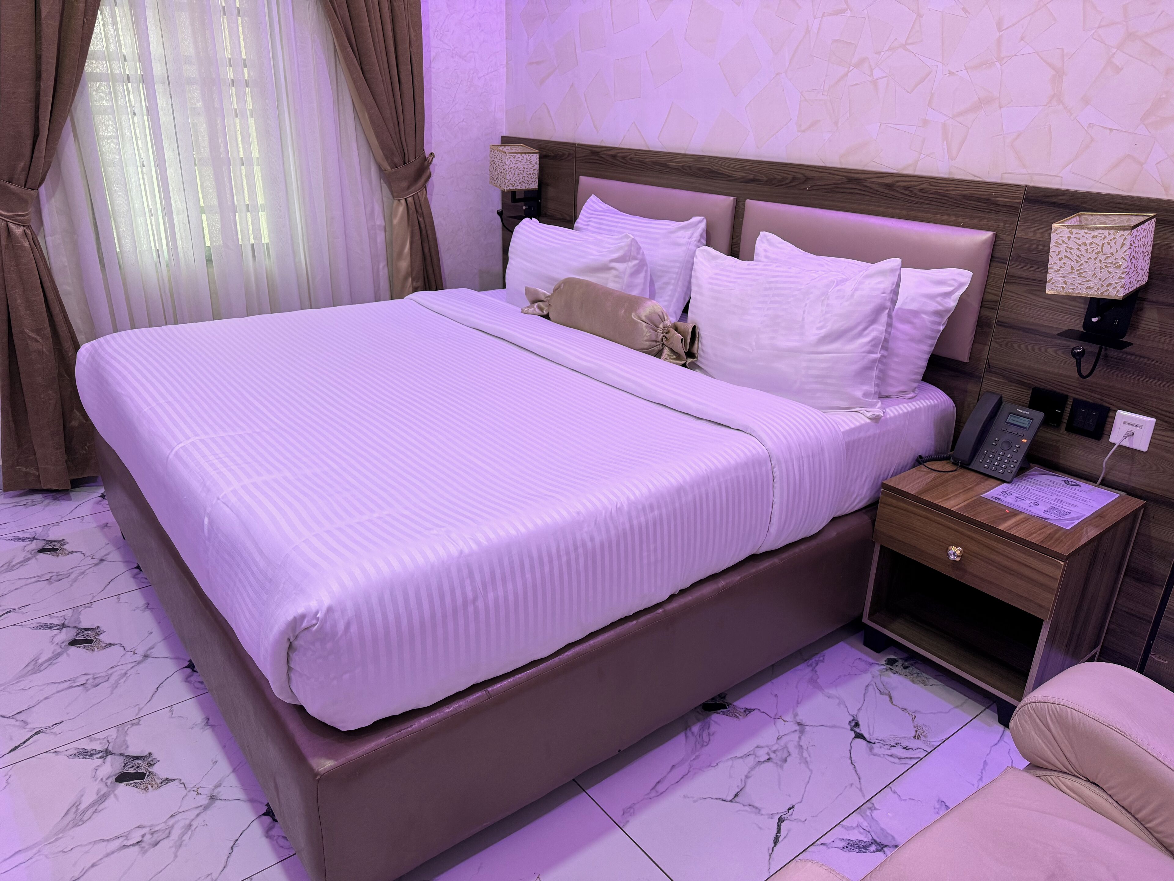 A hotel room with a large bed, a bedside table with a phone, and a nightstand with a lamp.