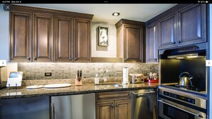 Eine moderne Küche mit Holzschränken, einer Granitabdeckung, Edelstahlgeräten und einer Spritzschutzwand.