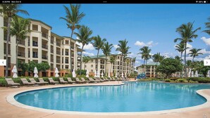 Ein Resort mit großem Pool, Palmen und einem mehrstöckigen Gebäude mit Balkonen.