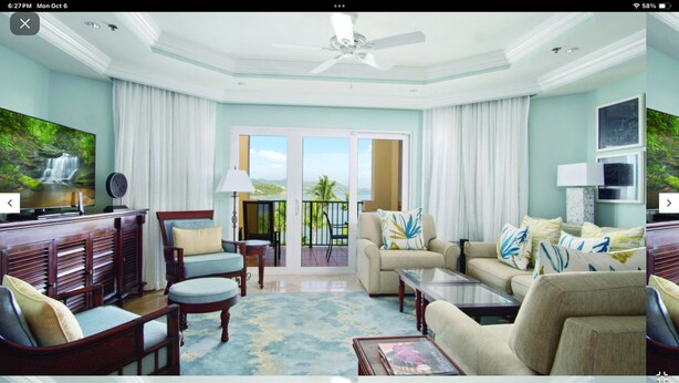 A spacious living room with a large TV, comfortable seating, and a balcony with a view.