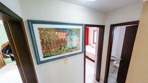 A hallway with a framed painting on the wall, a tiled floor, and a door leading to another room.
