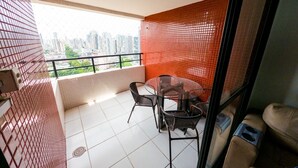 A balcony with a glass table and chairs, a red tiled wall, and a city view.