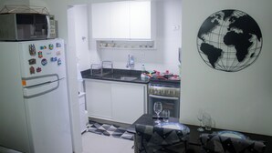 A compact kitchen with white cabinets, a microwave, a stove, and a dining area with a table set for two. - Cozy Copacabana - Apt 407 - three minutes from Brazil's most famous beach (Rio de Janeiro)