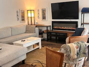 A living room with a sofa, a coffee table, a fireplace, a television, and decorative wall art.