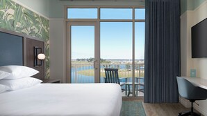 Une chambre d’hôtel avec un grand lit, un bureau avec une chaise, une télévision et un balcon offrant une vue sur la ville.