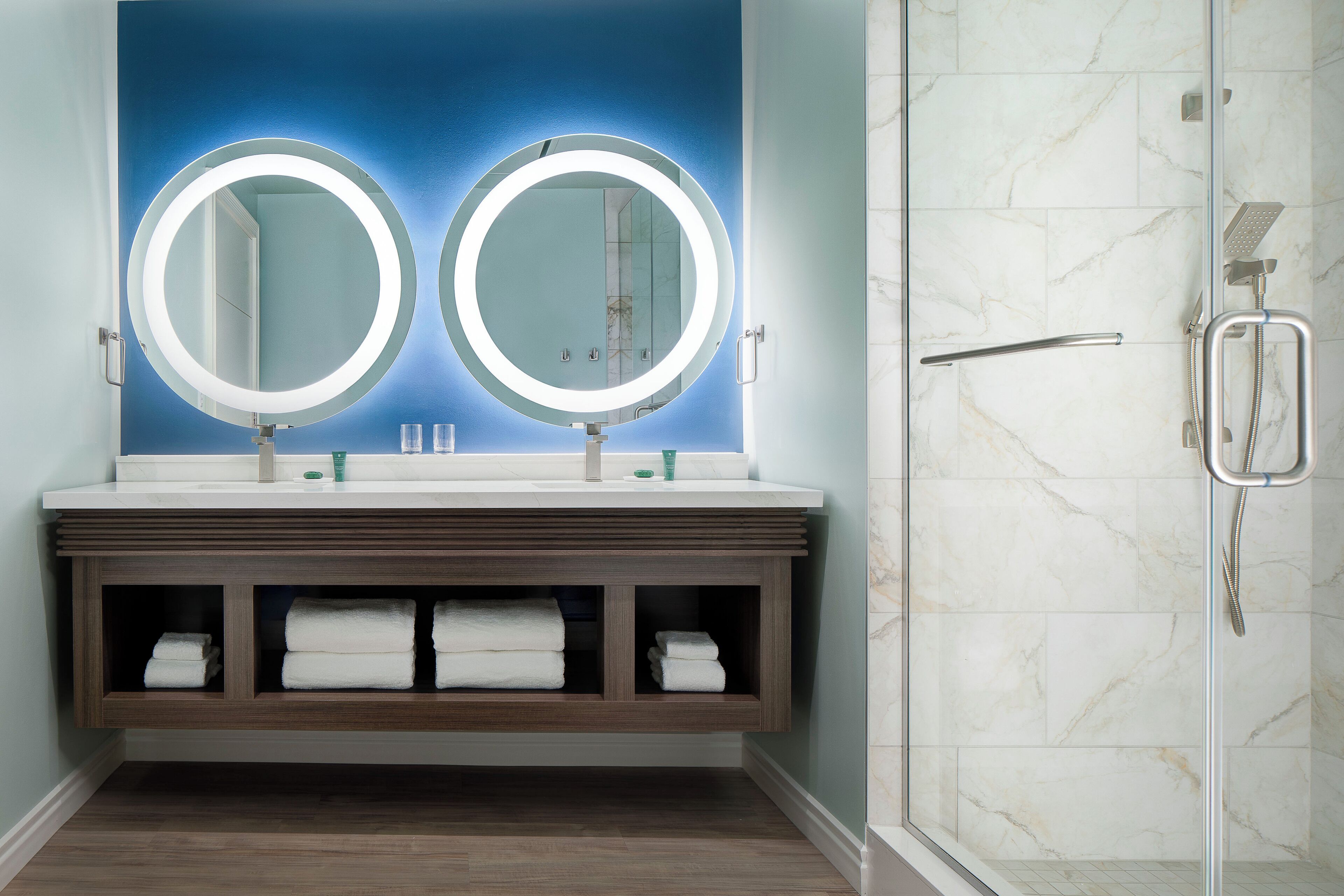 A bathroom with two round mirrors, a shower, and a marble wall.