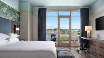 Habitación de hotel con una cama grande, un escritorio, una silla, televisión y un balcón con vistas.
