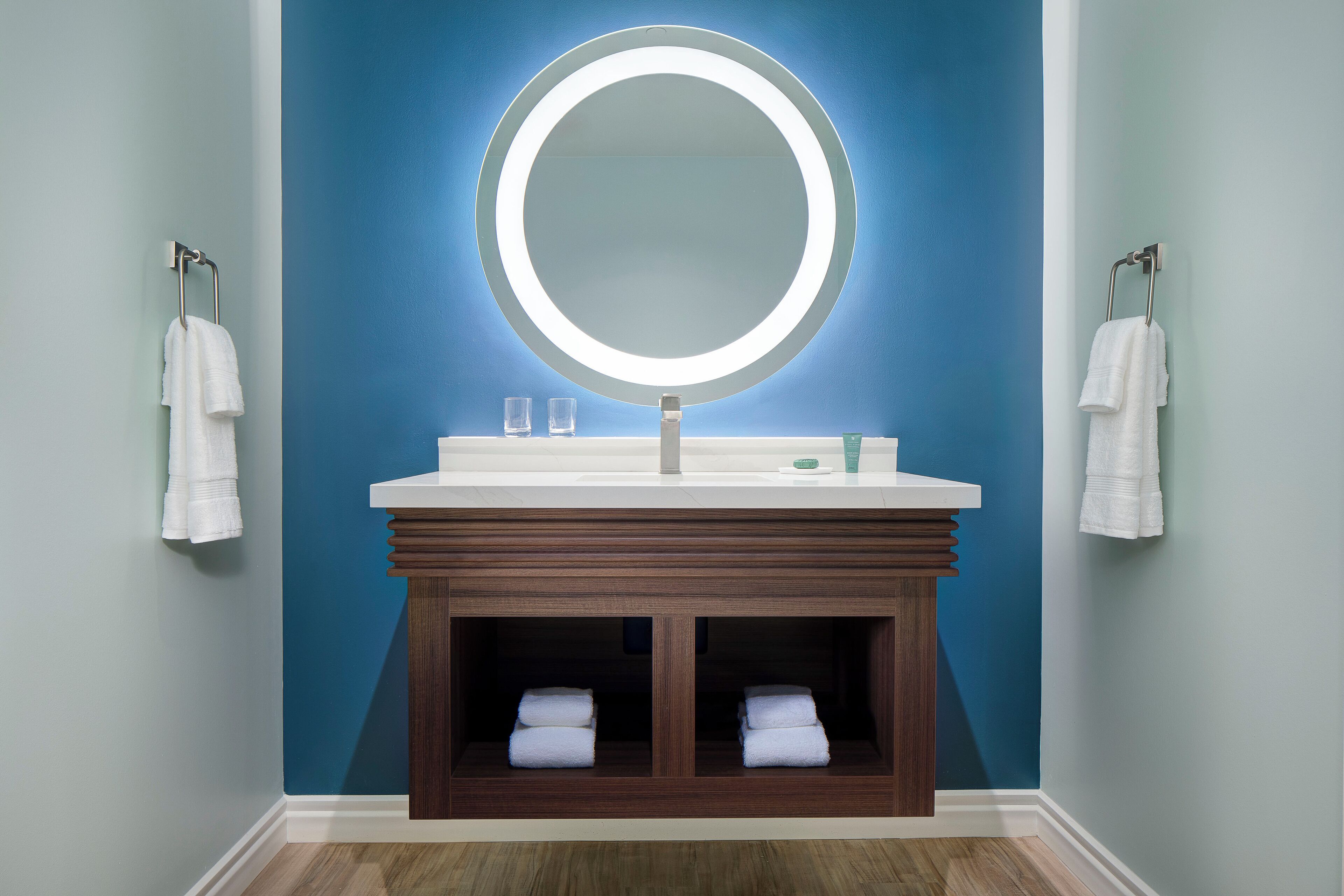 A bathroom with a round mirror, white sink, and two towel racks.