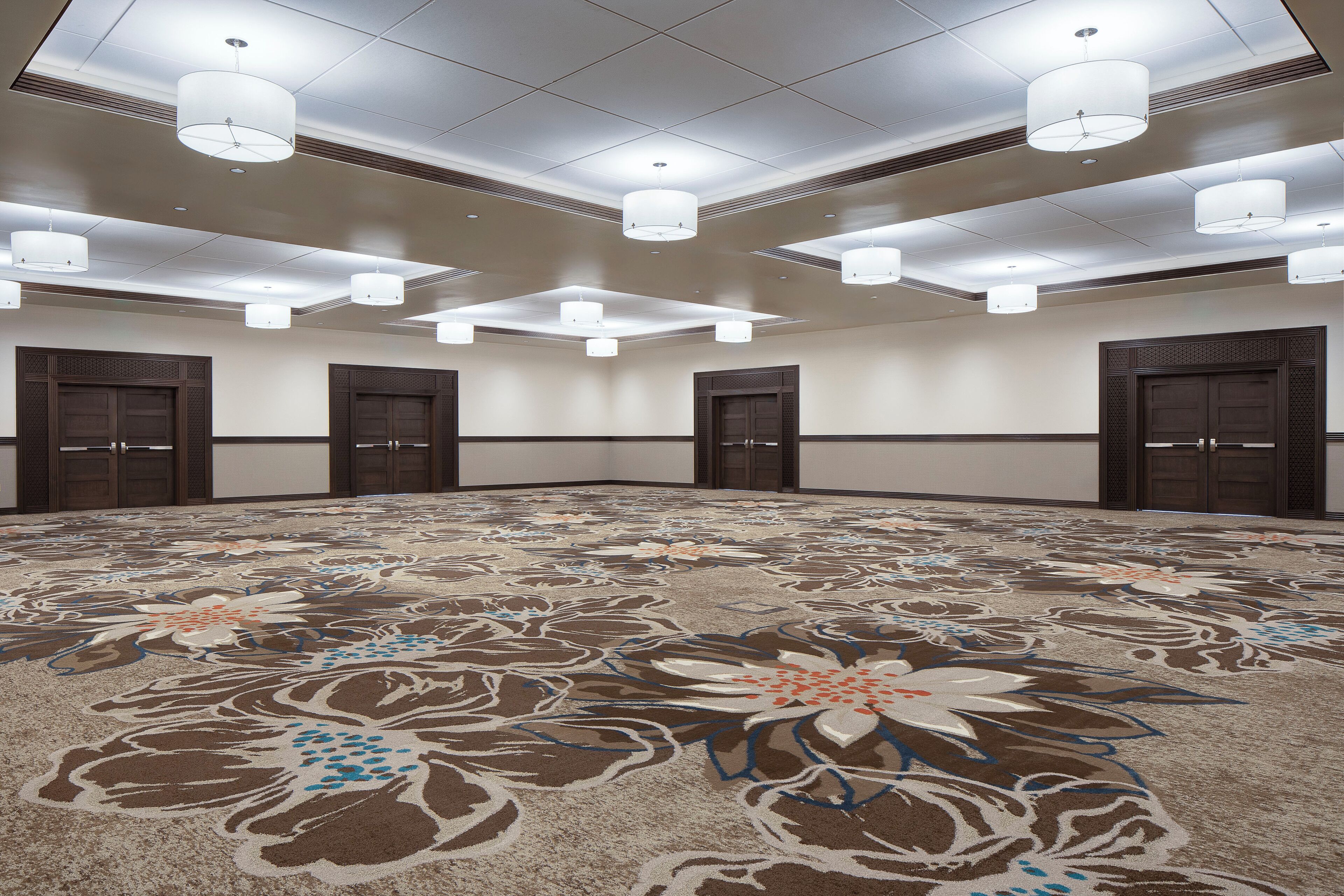 A large, carpeted room with a floral pattern, multiple doors, and ceiling lights.