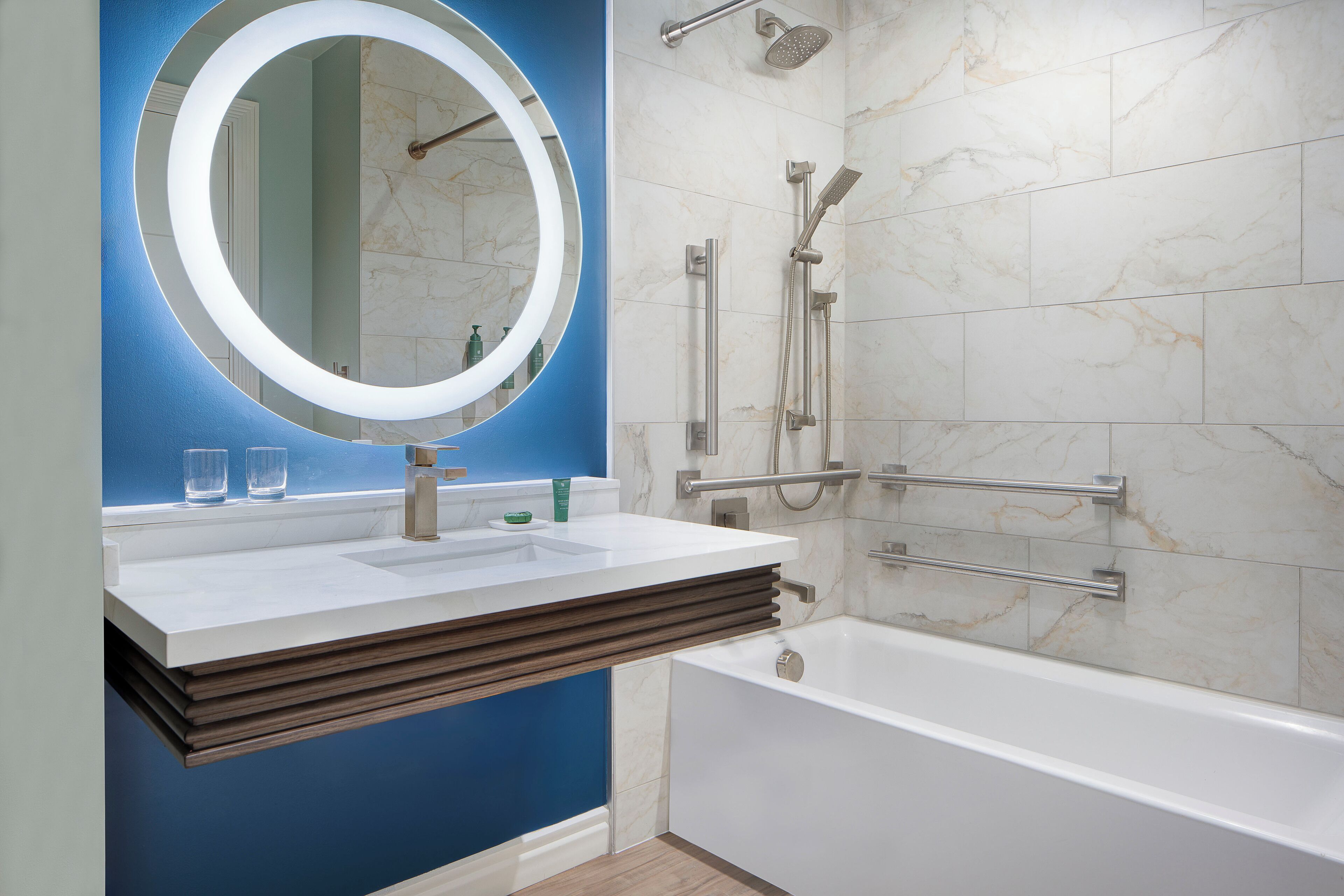 Un baño moderno con una bañera blanca, un espejo redondo con luz y una zona de ducha con cabezal de ducha manual.