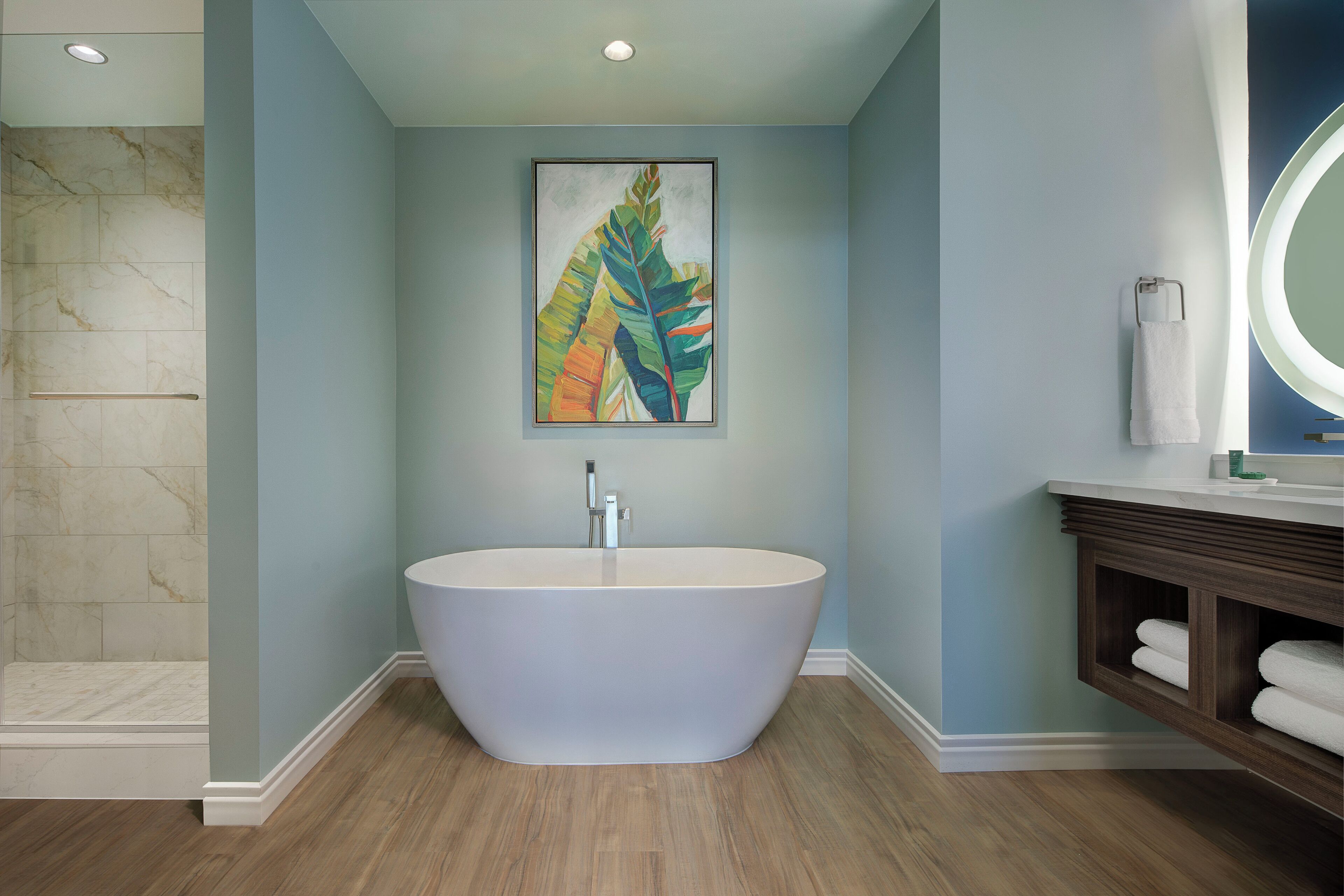 A modern bathroom with a freestanding bathtub, a marble shower wall, and a wooden vanity with a mirror.