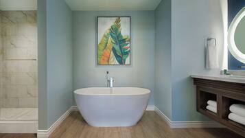 A modern bathroom with a freestanding bathtub, a marble shower wall, and a wooden vanity with a mirror.