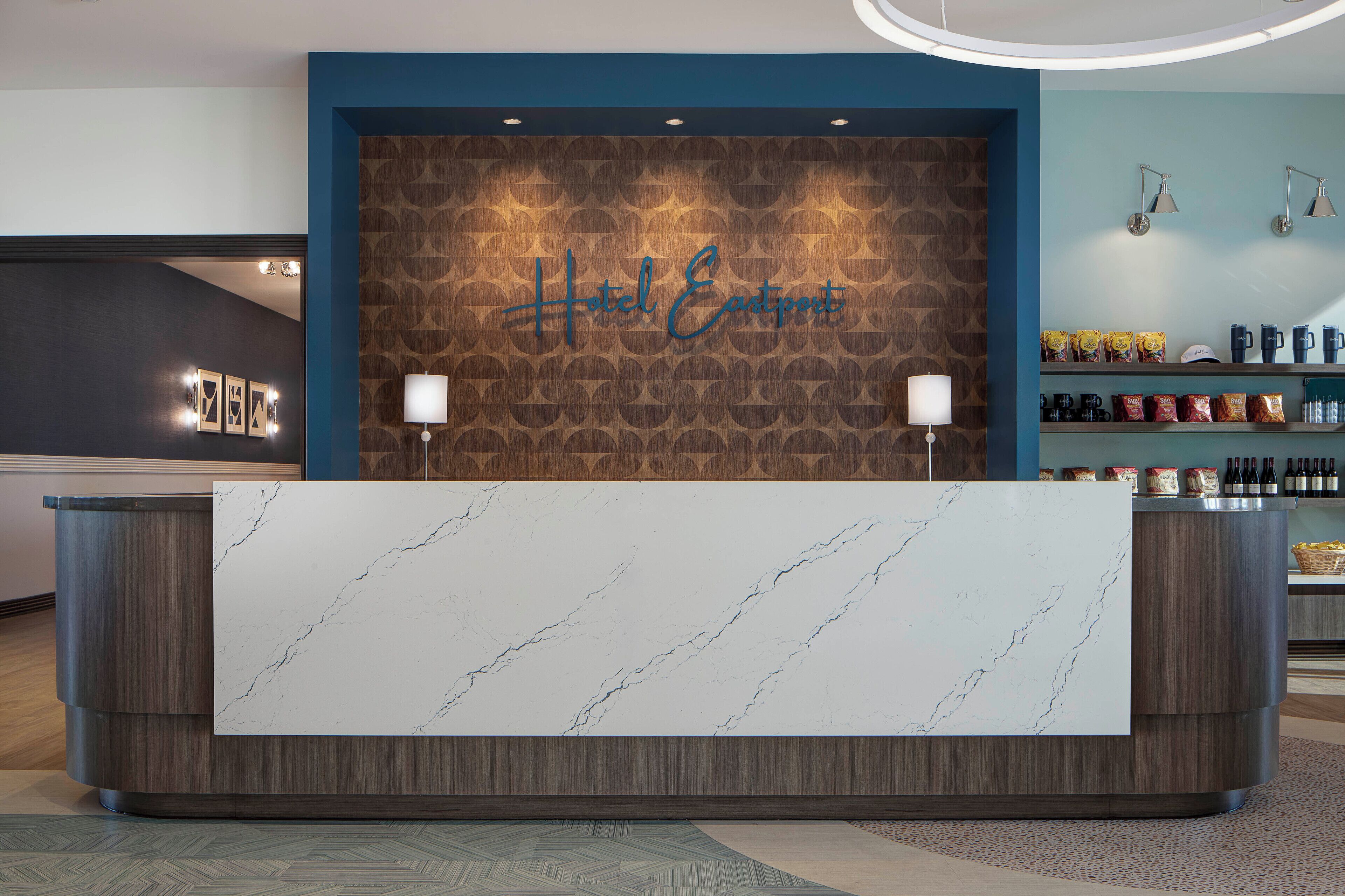 A hotel reception desk with a marble top, a wooden wall with a 'Hotel Eastpoint' sign, and a shelf with snacks and beverages.