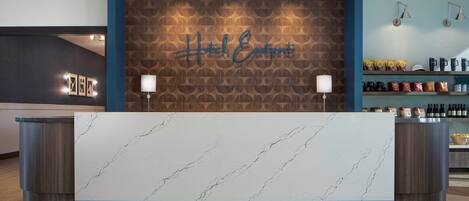A hotel reception desk with a marble top, a wooden wall with a 'Hotel Eastpoint' sign, and a shelf with snacks and beverages.
