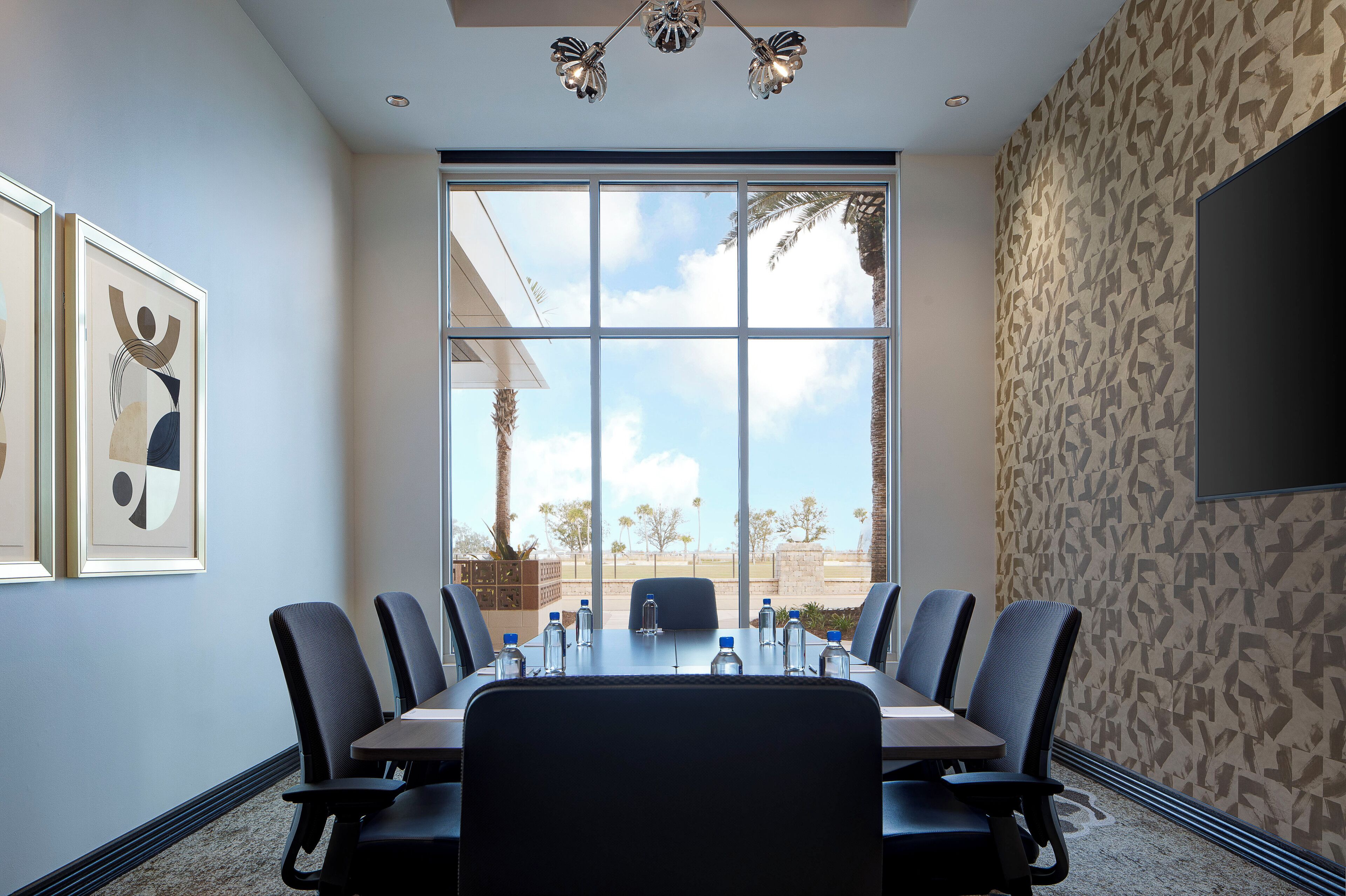 A conference room with a large table, chairs, and a view of palm trees through a large window.