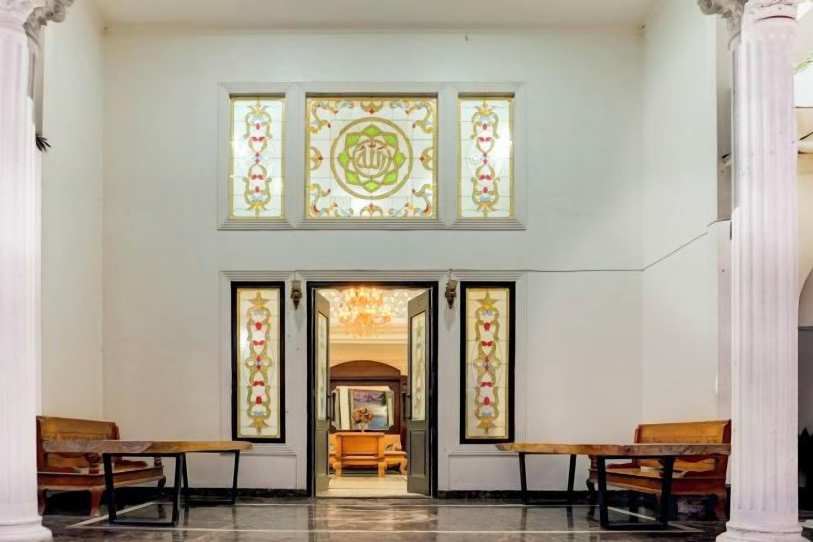 A lobby with a chandelier, benches, and a stained glass window.