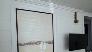 Quarto com uma grande moldura de fotografia de um veleiro em um corpo de água, uma televisão de tela plana presa na parede e uma porta que dá para outro quarto.